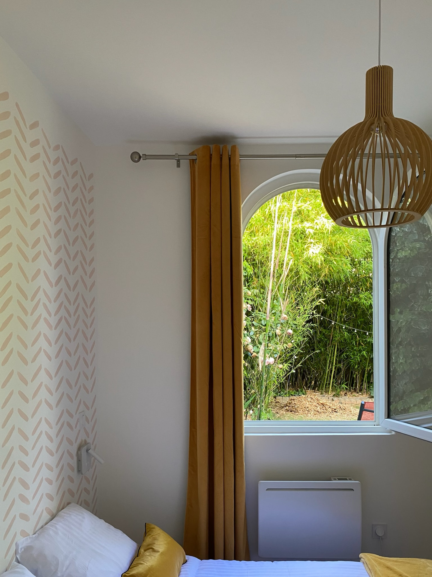 Chambre d’appartement rénové à Angers avec fenêtre en arc, rideaux moutarde et suspension en bois